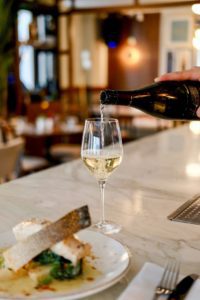 Un vin effervescent est versé dans un verre, accompagné d'un plat de poisson, illustrant les accords mets et vins pétillants en gastronomie.