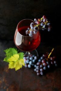 Verre de vin rouge aux reflets intenses posé à côté de grappes de raisins noirs, illustrant la richesse aromatique du vin.