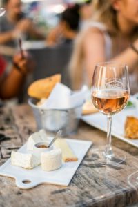 Un verre de vin rosé posé sur une table en terrasse, accompagné d'un plateau de fromages, illustrant un moment de dégustation convivial.