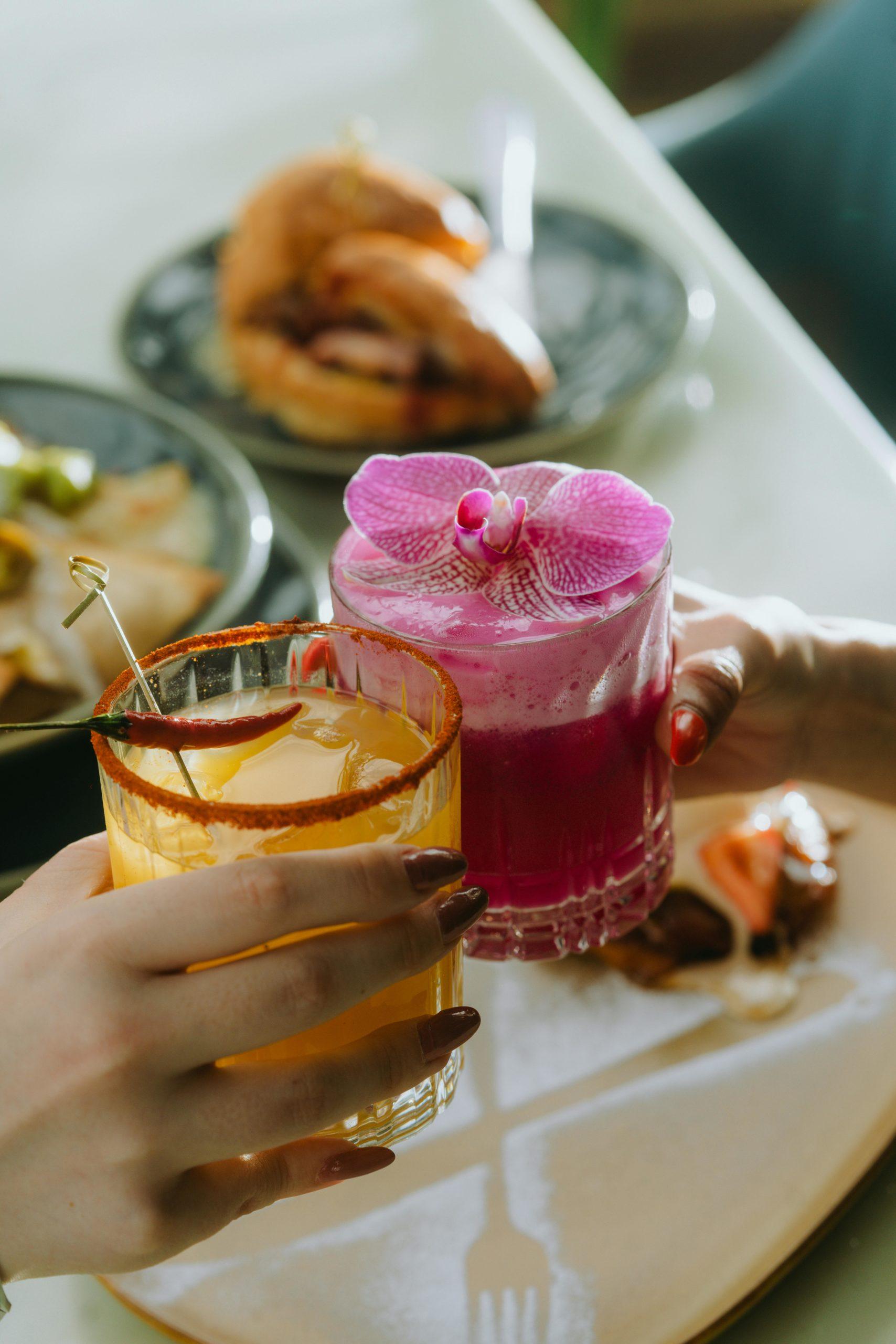 Image de deux cocktails fleuris tenus par deux mains.